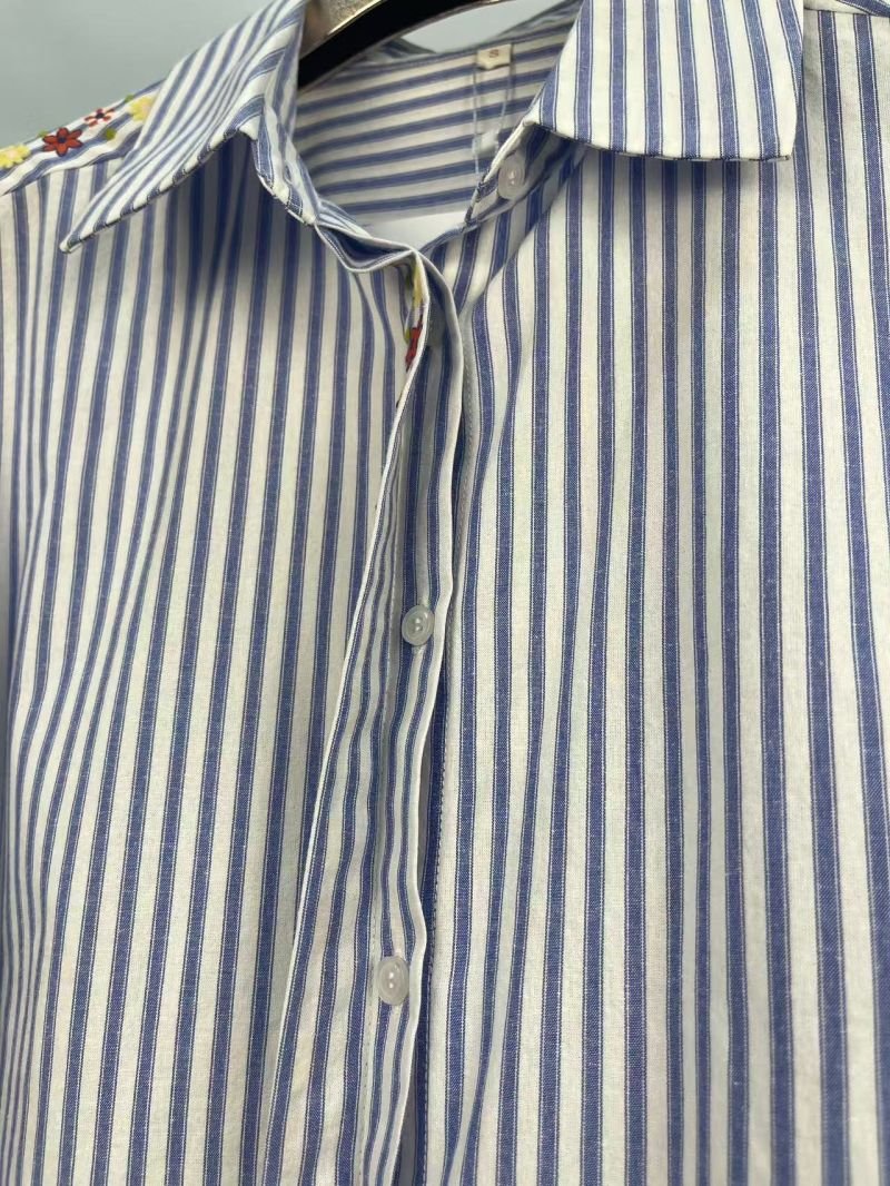 Striped Floral Detail Shirt in light blue and white. Macro close-up view focusing on the Blue-and-white vertical stripes with floral front detailing. B2B wholesale Blouses & Tops SKU: AM260953.